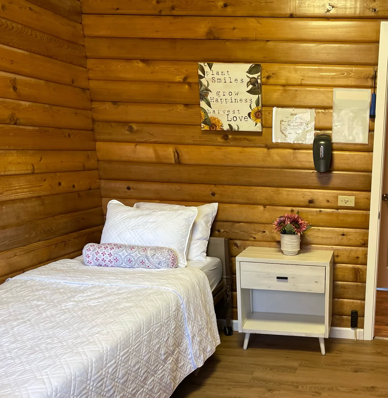 A resident bedroom with log walls and fresh flowers at Birdsong Adult Family Home, Kent WA